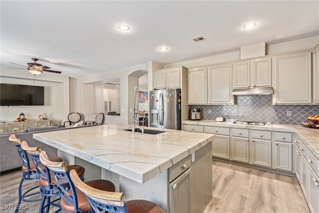 kitchen featuring light stone countertops, appliances with stainless steel finishes, a kitchen breakfast bar, a center island with sink, and light hardwood / wood-style flooring