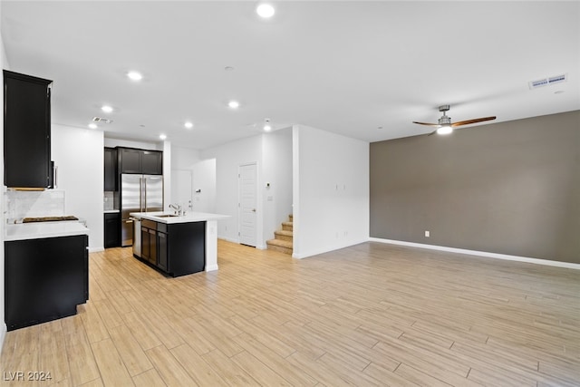 kitchen featuring ceiling fan, sink, light hardwood / wood-style flooring, stainless steel refrigerator, and an island with sink