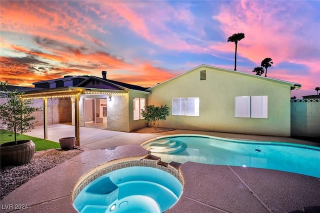 pool at dusk with a patio area and an in ground hot tub