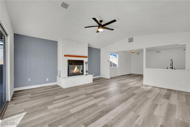 unfurnished living room with a fireplace, ceiling fan, vaulted ceiling, and light wood-type flooring