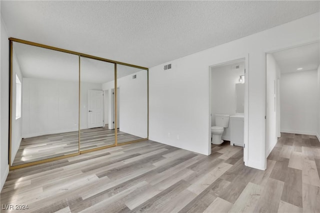 interior space featuring ensuite bathroom, a closet, a textured ceiling, and light hardwood / wood-style flooring