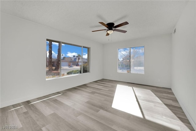 empty room with ceiling fan, light wood-type flooring, and a textured ceiling