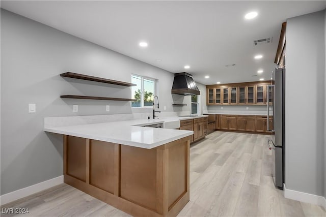 kitchen featuring light wood finished floors, visible vents, a sink, ventilation hood, and a peninsula