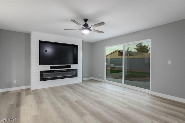 unfurnished living room featuring ceiling fan, baseboards, a large fireplace, and wood finished floors