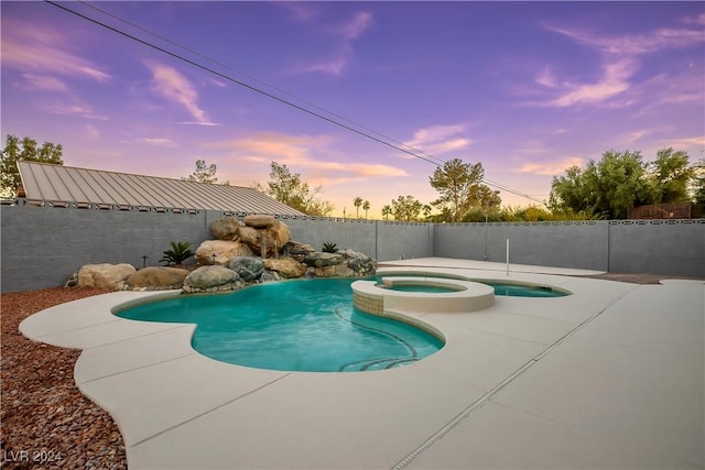 pool at dusk with a pool with connected hot tub, fence, and a patio