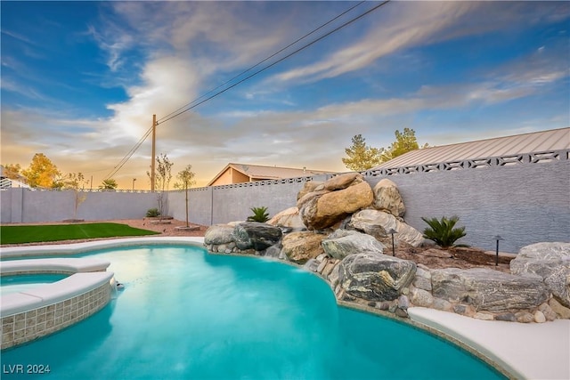 pool at dusk featuring a pool with connected hot tub and a fenced backyard