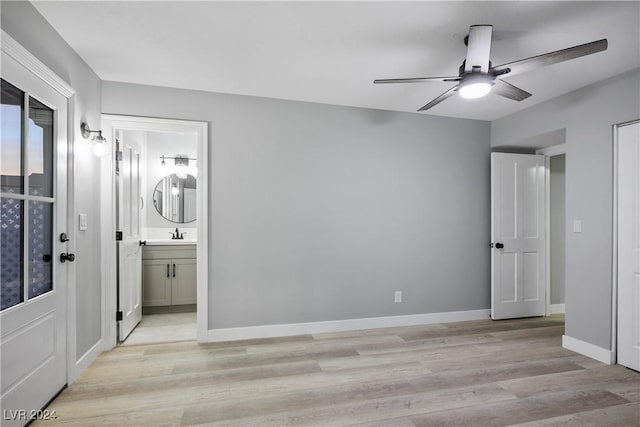 unfurnished bedroom featuring a sink, ensuite bathroom, light wood finished floors, ceiling fan, and baseboards