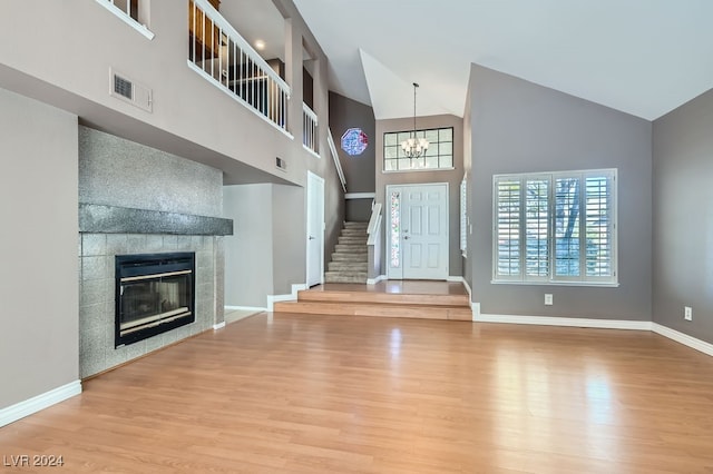 unfurnished living room with a chandelier, a tile fireplace, high vaulted ceiling, and light hardwood / wood-style flooring