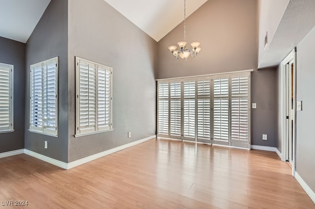 spare room with high vaulted ceiling, a chandelier, and light hardwood / wood-style floors