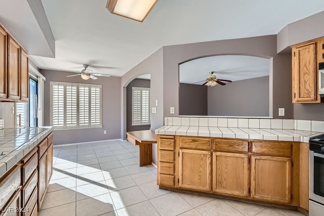 kitchen with tile countertops, ceiling fan, light tile patterned floors, and electric range