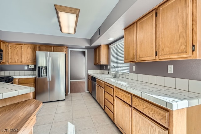 kitchen featuring tile countertops, sink, light tile patterned flooring, and appliances with stainless steel finishes