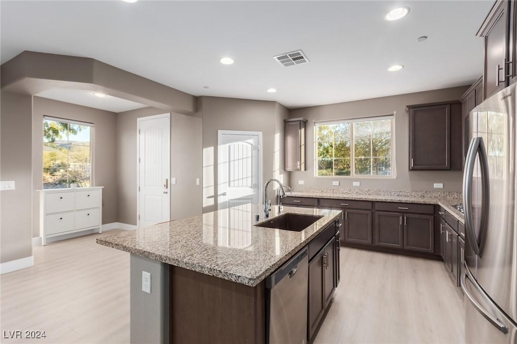 kitchen with light stone countertops, sink, stainless steel appliances, an island with sink, and light hardwood / wood-style floors