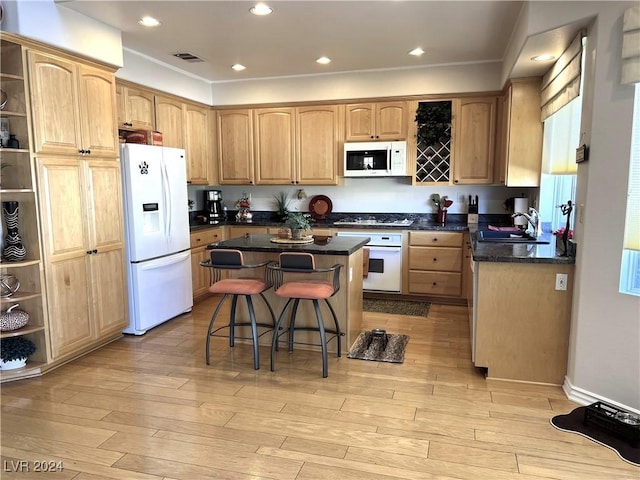 kitchen featuring a breakfast bar, white appliances, sink, light hardwood / wood-style flooring, and a center island