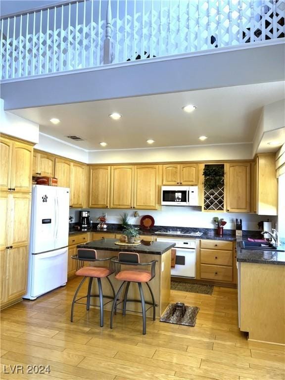 kitchen with a towering ceiling, light hardwood / wood-style floors, white appliances, a breakfast bar area, and a kitchen island