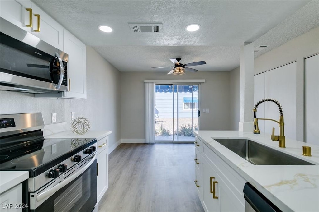 kitchen featuring sink, light hardwood / wood-style flooring, a textured ceiling, white cabinets, and appliances with stainless steel finishes