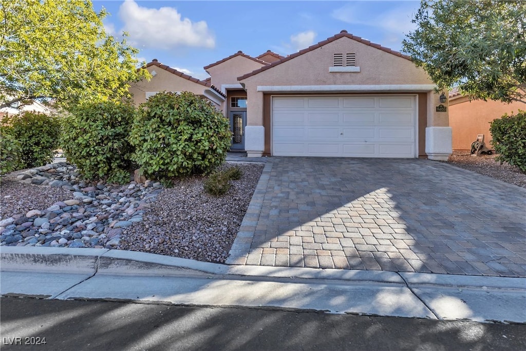 view of front facade with a garage, decorative driveway, a tiled roof, and stucco siding