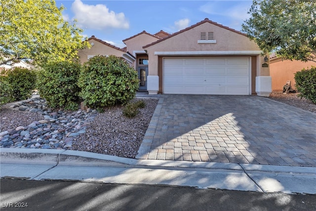 view of front facade with a garage, decorative driveway, a tiled roof, and stucco siding