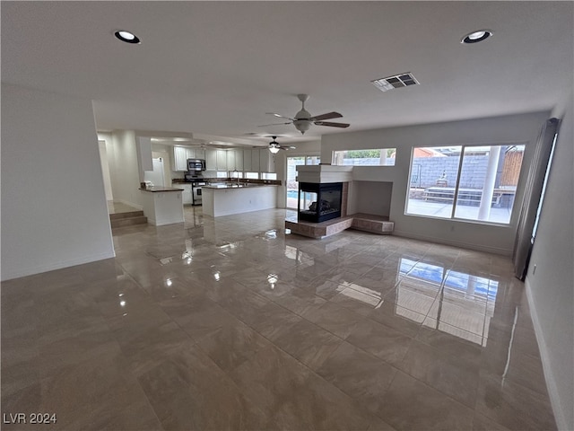 unfurnished living room featuring ceiling fan and a multi sided fireplace