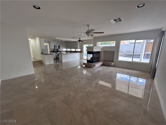 unfurnished living room featuring a multi sided fireplace and ceiling fan