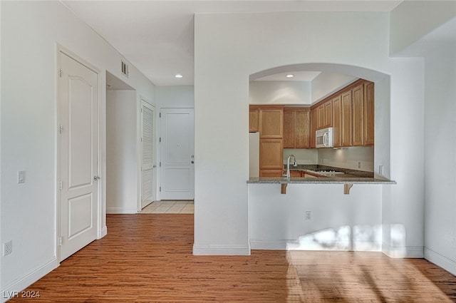 kitchen featuring kitchen peninsula, light wood-type flooring, white appliances, sink, and a breakfast bar area