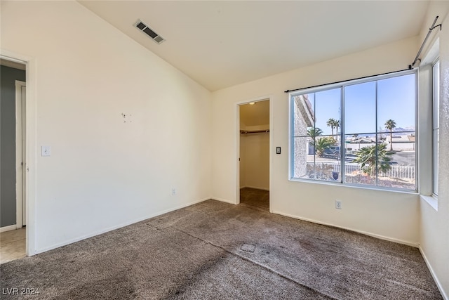 unfurnished bedroom featuring a walk in closet, a closet, carpet floors, and lofted ceiling