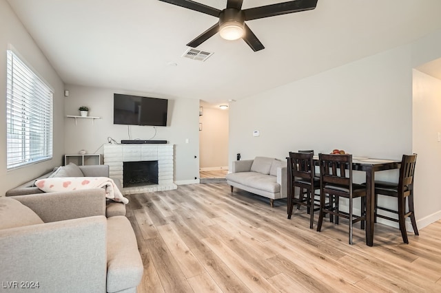 living room featuring ceiling fan, light hardwood / wood-style flooring, and a brick fireplace