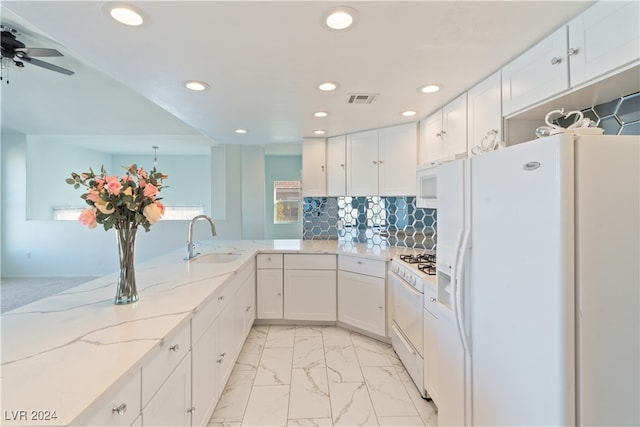 kitchen with light stone countertops, kitchen peninsula, white appliances, sink, and white cabinetry