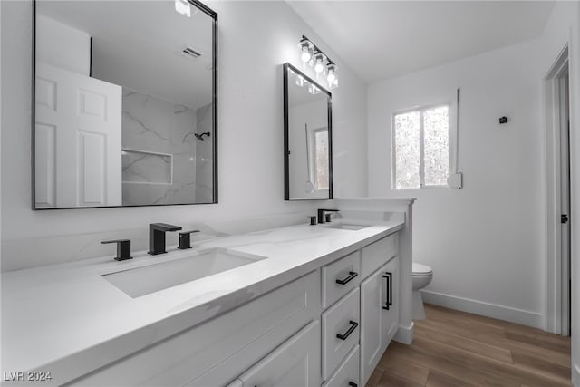 bathroom featuring a tile shower, vanity, hardwood / wood-style flooring, and toilet