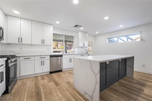 kitchen with light stone countertops, appliances with stainless steel finishes, a kitchen island, light hardwood / wood-style floors, and white cabinetry