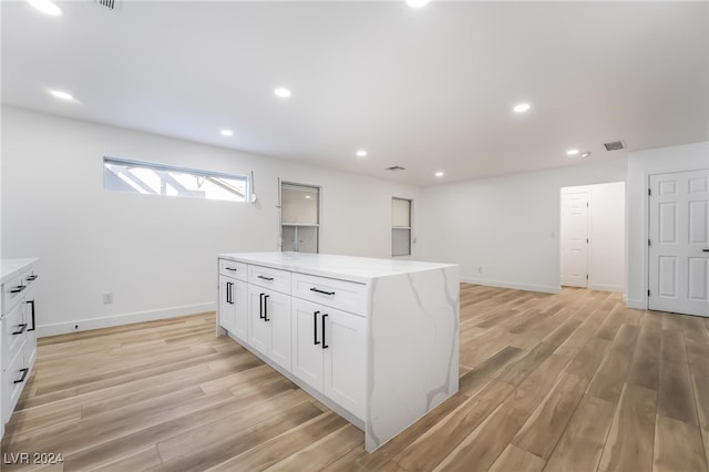 kitchen with white cabinets, light stone countertops, light hardwood / wood-style flooring, and a kitchen island