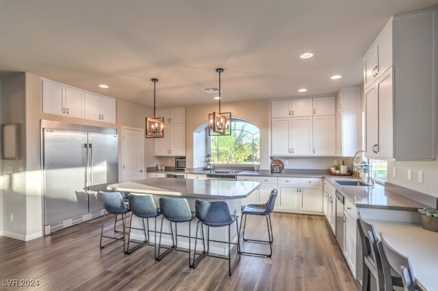 kitchen featuring dark wood-type flooring, hanging light fixtures, white cabinets, a kitchen island, and appliances with stainless steel finishes