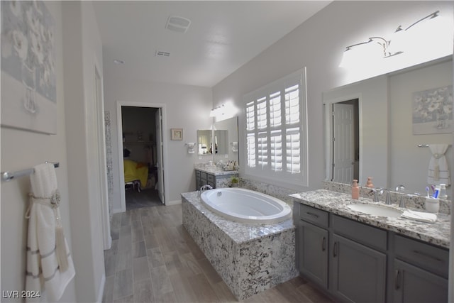 bathroom featuring hardwood / wood-style floors, vanity, and a relaxing tiled tub