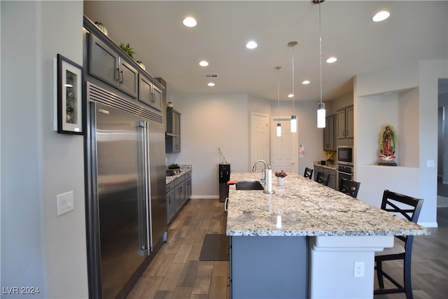 kitchen with dark hardwood / wood-style flooring, built in appliances, pendant lighting, a spacious island, and a breakfast bar