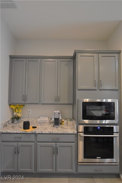 kitchen with gray cabinets, light stone counters, and stainless steel oven