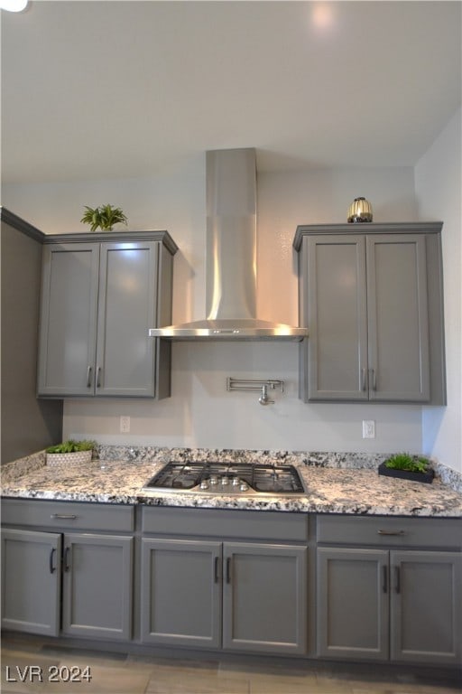 kitchen featuring light stone countertops, gray cabinets, stainless steel gas stovetop, and wall chimney range hood