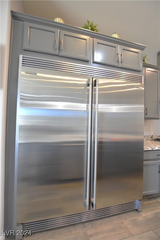 details with hardwood / wood-style floors, gray cabinets, stainless steel built in fridge, and light stone counters