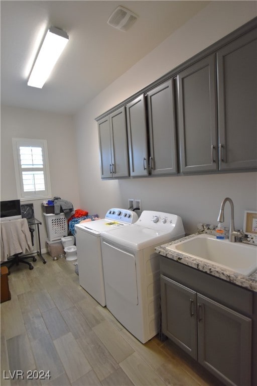 laundry room featuring washing machine and dryer, sink, cabinets, and light wood-type flooring