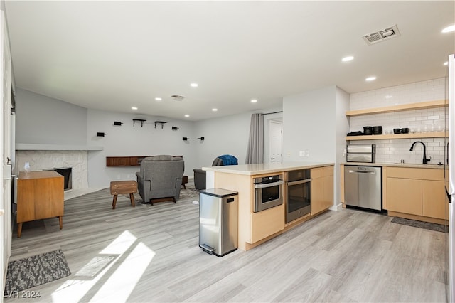 kitchen with kitchen peninsula, sink, appliances with stainless steel finishes, and light hardwood / wood-style flooring