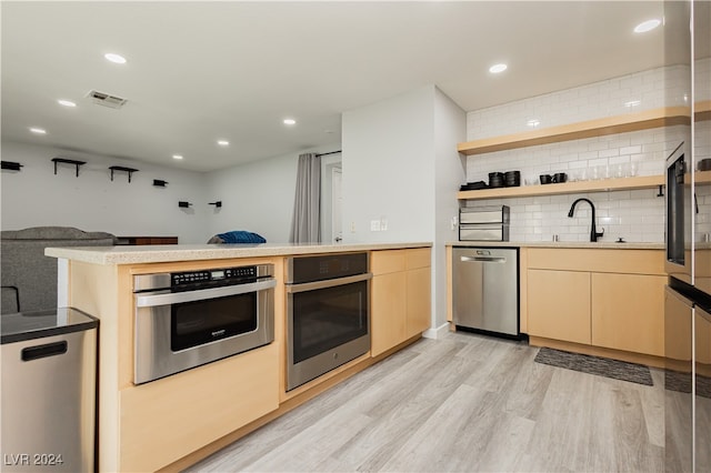 kitchen featuring sink, light hardwood / wood-style flooring, kitchen peninsula, decorative backsplash, and appliances with stainless steel finishes