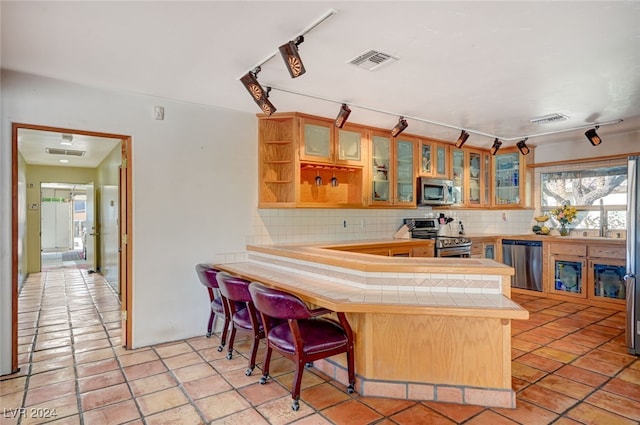 kitchen featuring tile countertops, a kitchen breakfast bar, appliances with stainless steel finishes, tasteful backsplash, and kitchen peninsula