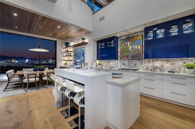 kitchen featuring light wood-type flooring, blue cabinets, decorative light fixtures, a center island, and white cabinetry