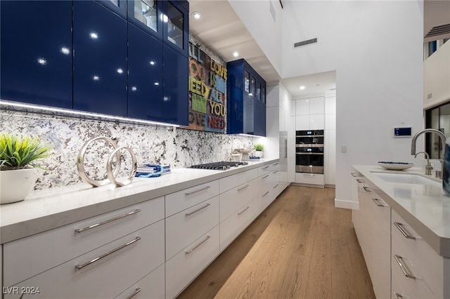 kitchen with white cabinetry, sink, blue cabinets, backsplash, and light hardwood / wood-style floors