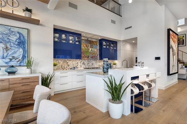 bar with white cabinets, sink, a towering ceiling, blue cabinetry, and light hardwood / wood-style floors