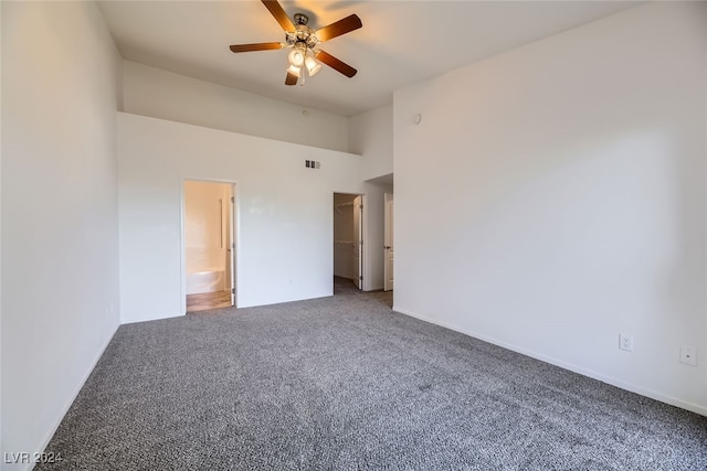 unfurnished bedroom featuring ceiling fan, carpet floors, ensuite bathroom, and a high ceiling