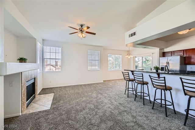 kitchen with hanging light fixtures, stainless steel refrigerator with ice dispenser, light colored carpet, a kitchen bar, and a fireplace