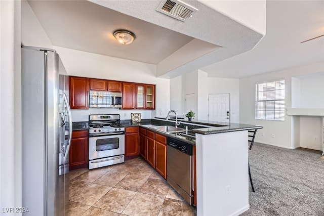 kitchen with sink, stainless steel appliances, kitchen peninsula, dark stone counters, and a kitchen bar