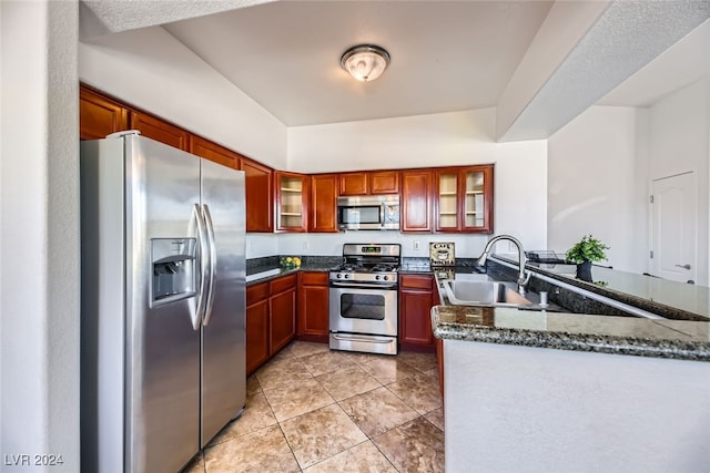 kitchen with sink, kitchen peninsula, dark stone countertops, light tile patterned floors, and appliances with stainless steel finishes