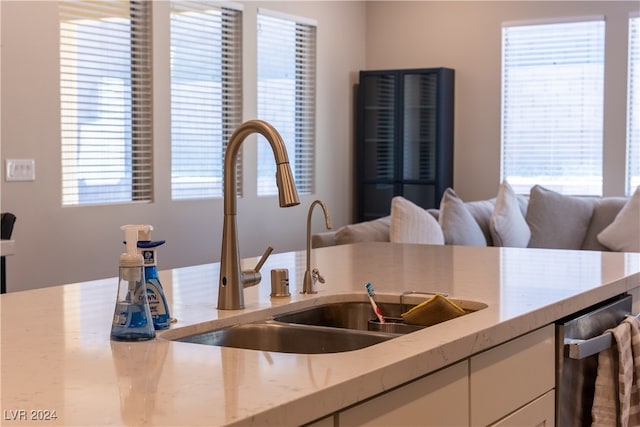 kitchen with light stone counters, white cabinetry, and sink