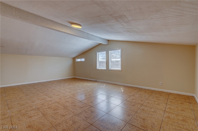 additional living space featuring vaulted ceiling with beams, light tile patterned floors, and a textured ceiling