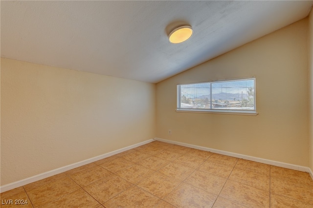 tiled spare room featuring vaulted ceiling